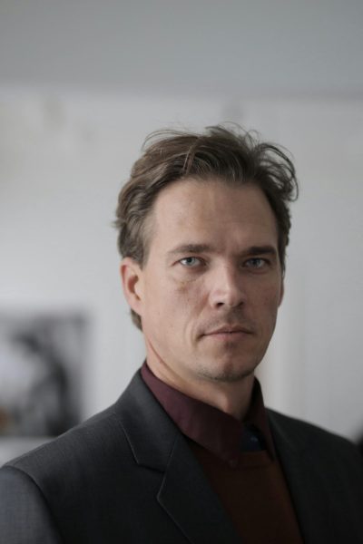 Confident businessman in a formal suit posing indoors with a serious expression.
